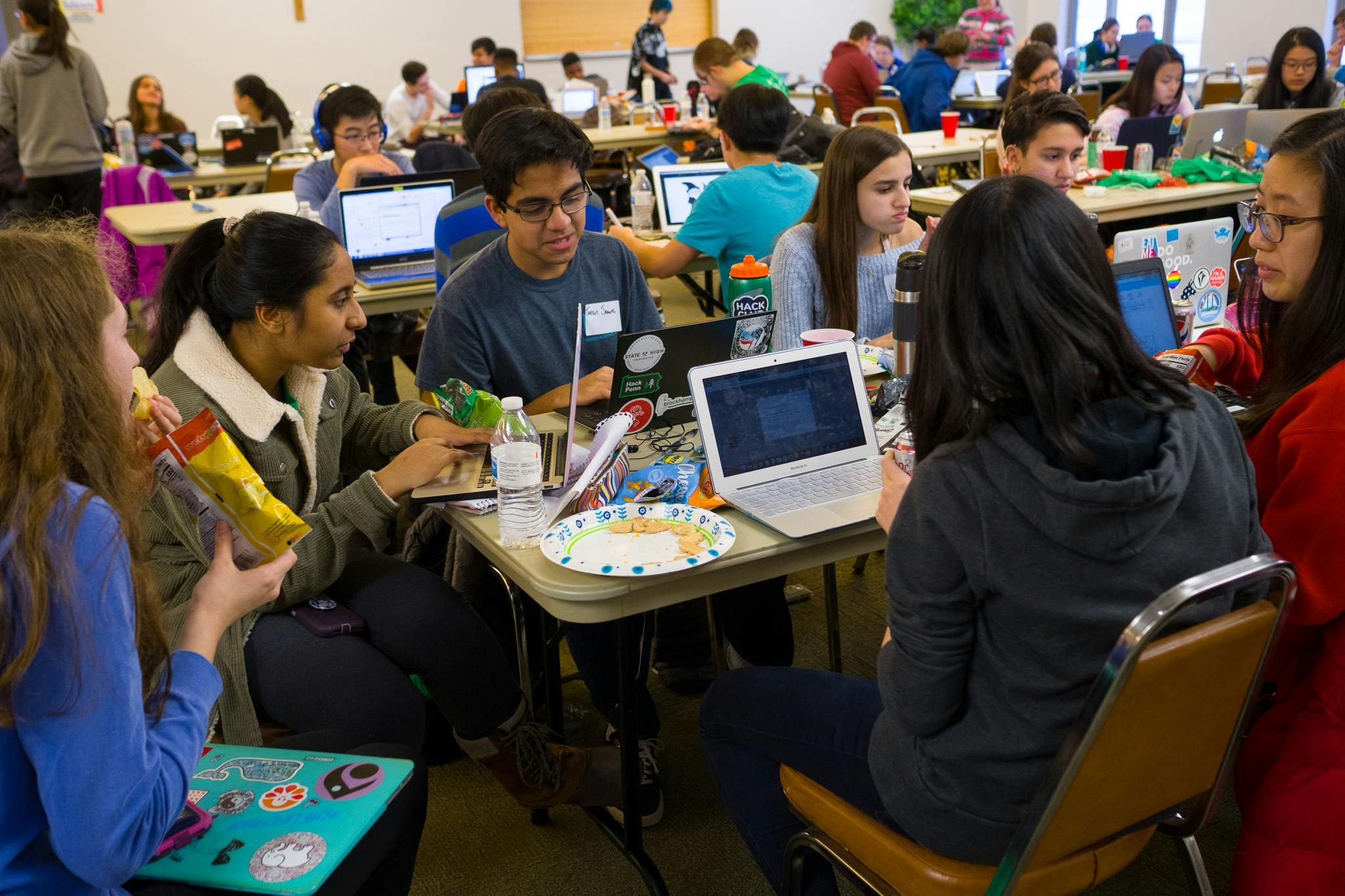 Team of students working on coding a project, surrounded by other students